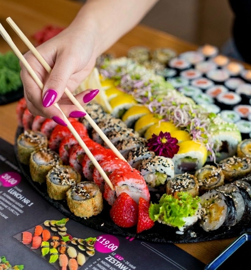 Okrągła taca sushi Nova Sushi, gość sięga pałeczkami po rolkę z truskawką